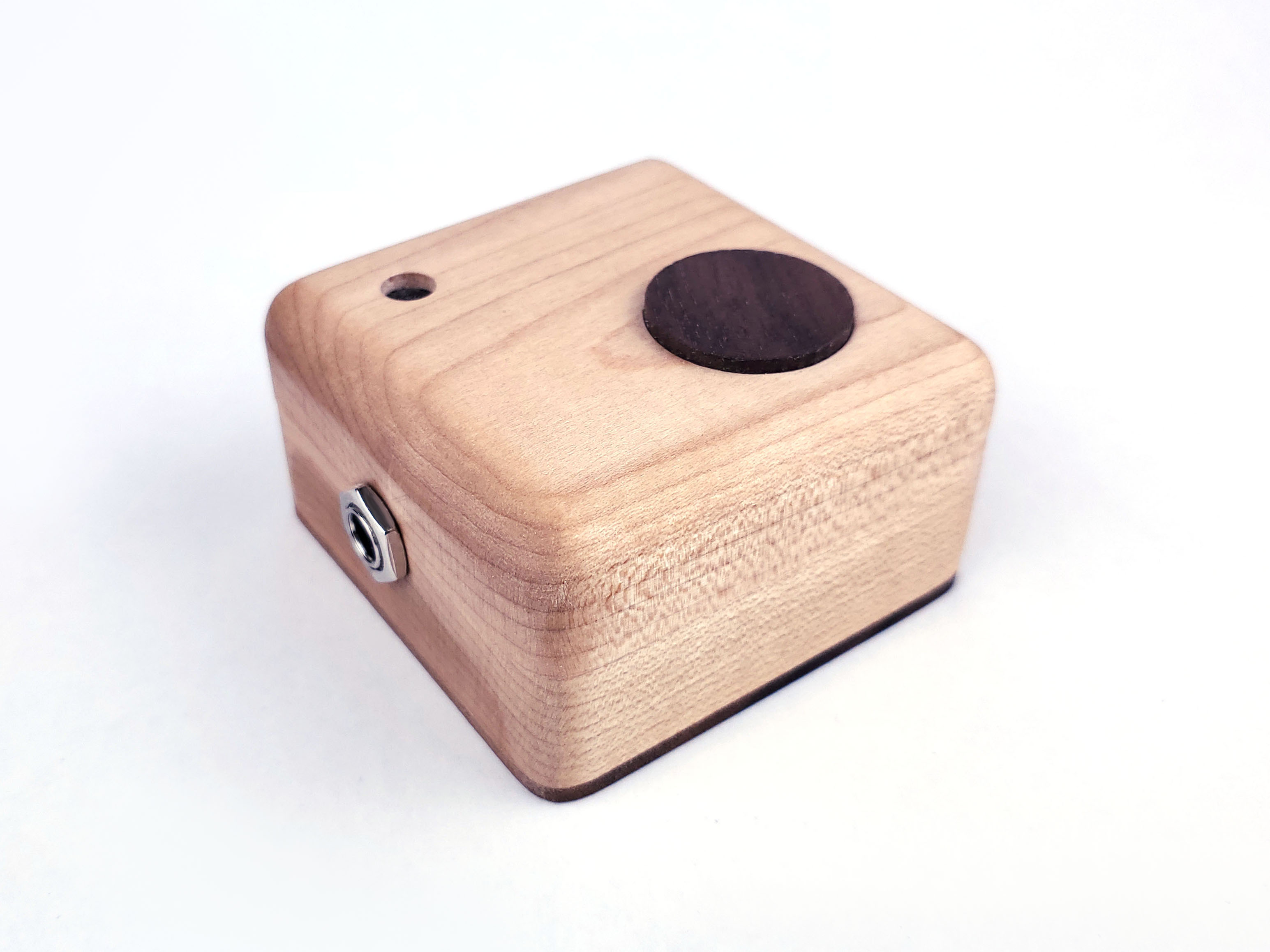 Smooth wooden instrument with a button, audio jack, and small window/lens